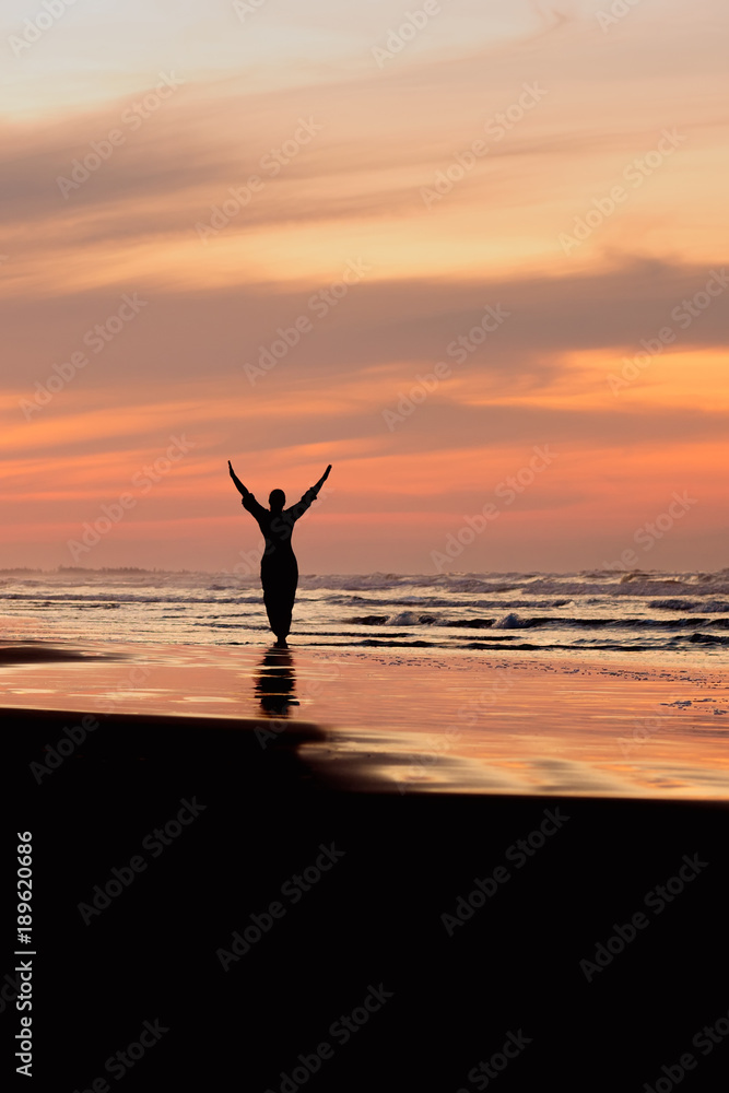 Silhouette of a woman with hands up at sunset
