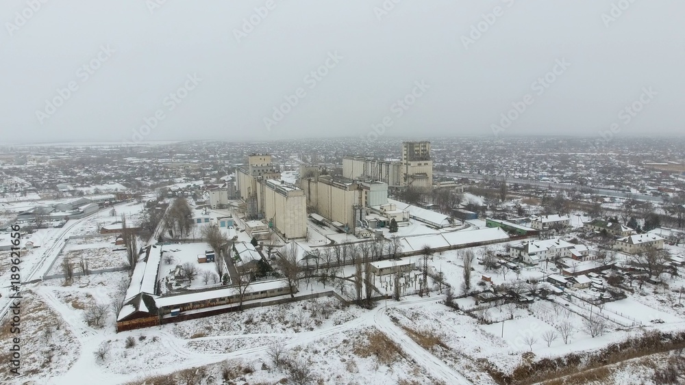 Fototapeta premium Grain terminal in the winter season. Snow-covered grain elevator in rural areas. A building for drying and storing grain