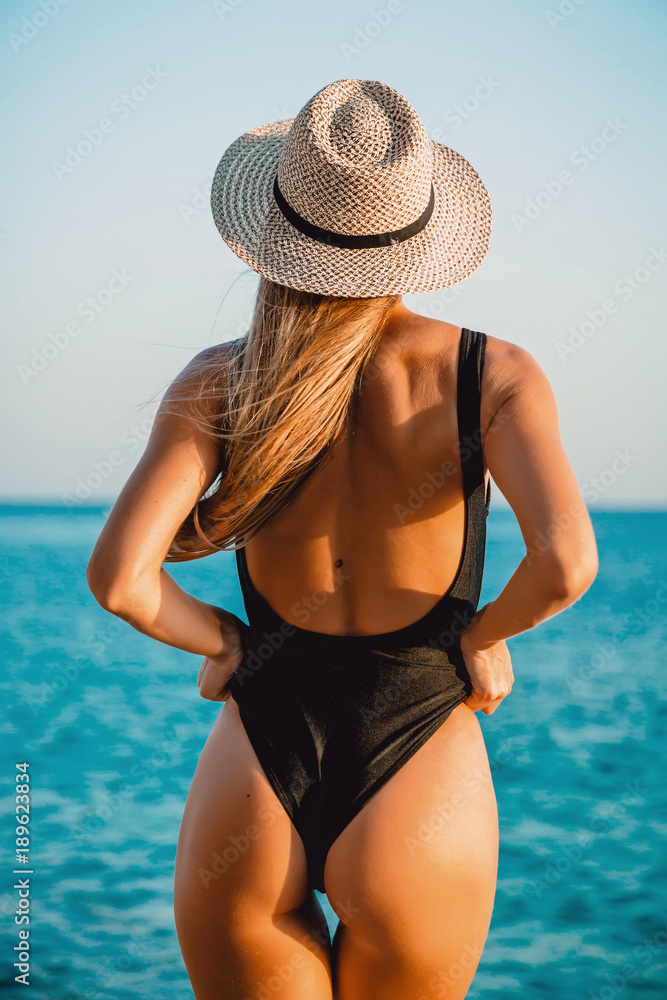 Back view of attractive woman in bikini with bonnet relaxing at sea