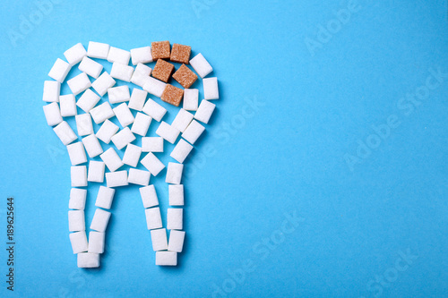 Sugar destroys the tooth enamel and leads to tooth decay. Sugar cubes are laid out in the form of a tooth and brown sugar symbolizes caries. Copy space for text