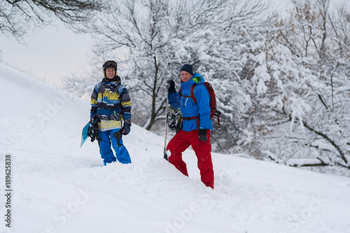 Two happy snowboarders are standing in the forest