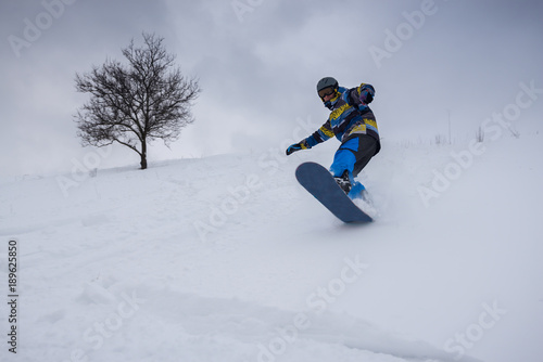 Snowboarder is jumping while riding along the forest slope
