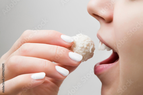 Woman eating a white coconut ball on the gray background. Enjoying sweets concept. photo