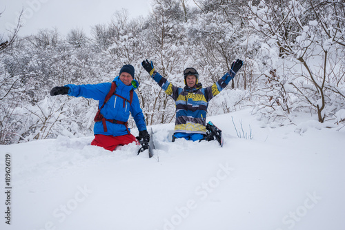 Two cheerful snowboarders are sitting in deep snow