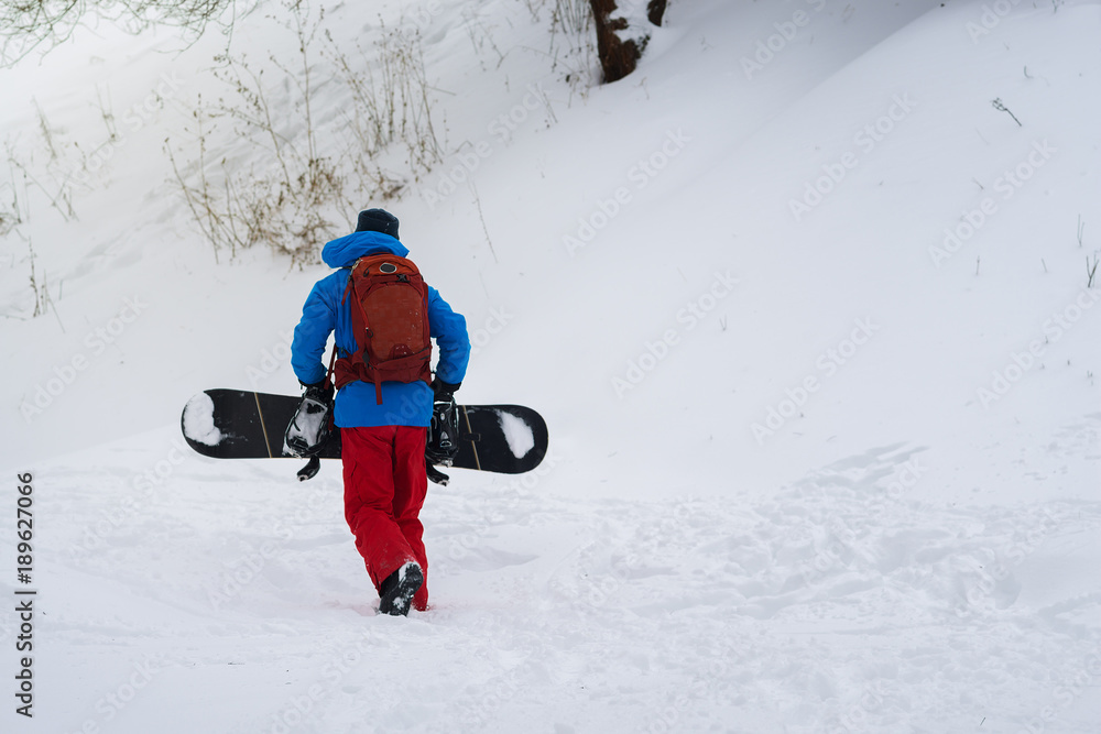 Snowboarder with backpack climbs up the slope