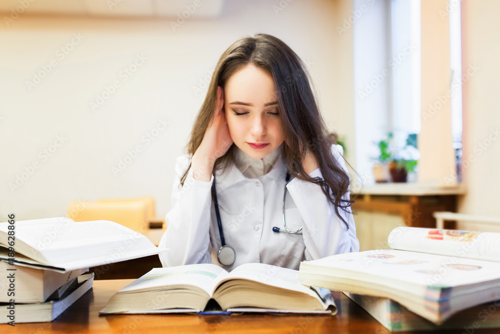A female medical student with a headache is studying a new topic on textbooks. A female medical student with a headache is studying a new topic on textbooks.