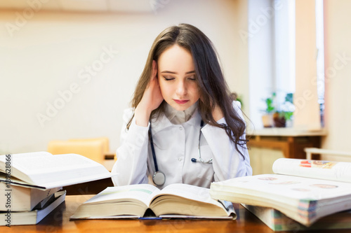 A female medical student with a headache is studying a new topic on textbooks.