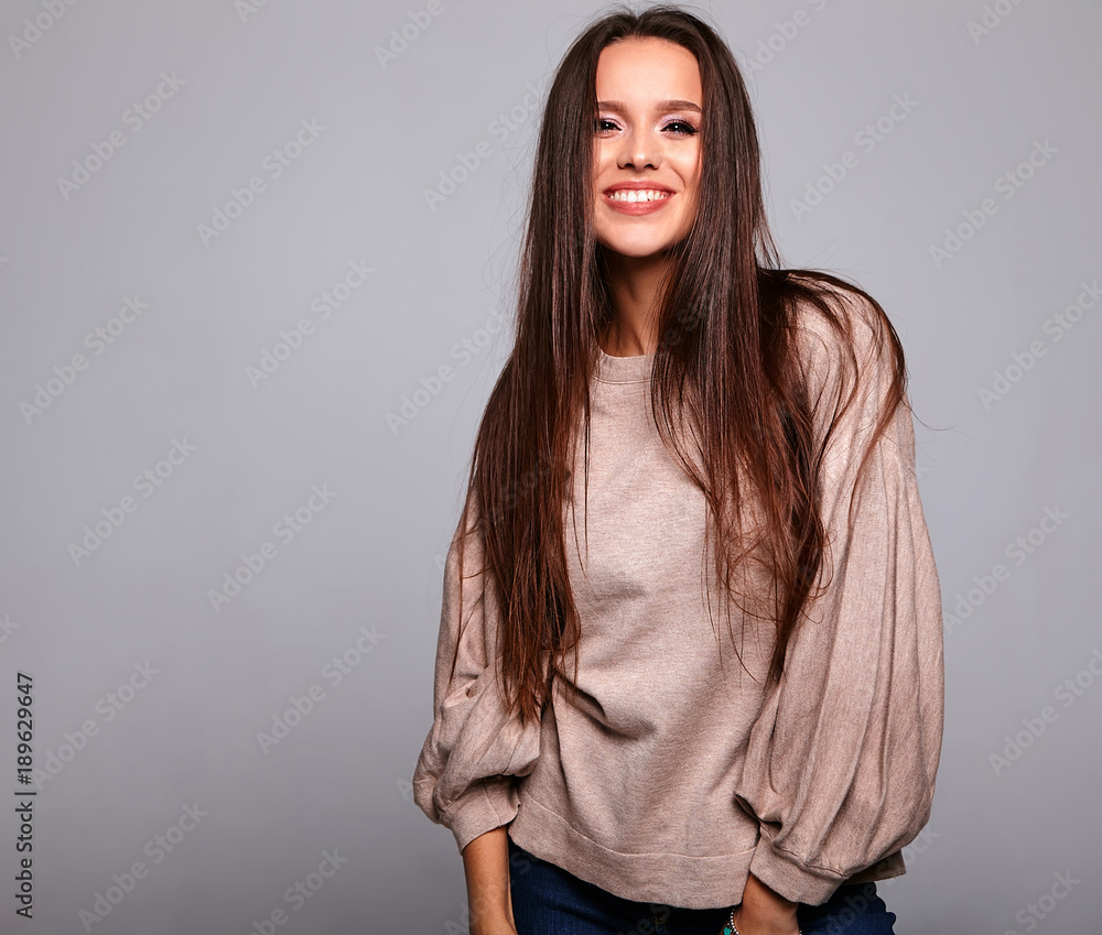 Portrait of beautiful smiling cute brunette woman model in casual beige warm sweater clothes with no makeup isolated on gray Portrait of beautiful smiling cute brunette woman model in casual beige warm sweater clothes with no makeup isolated on gray