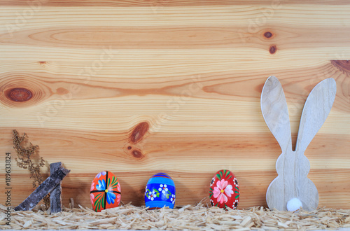 Osterarragement vor einer Holzwand bunte Ostereier, Hase