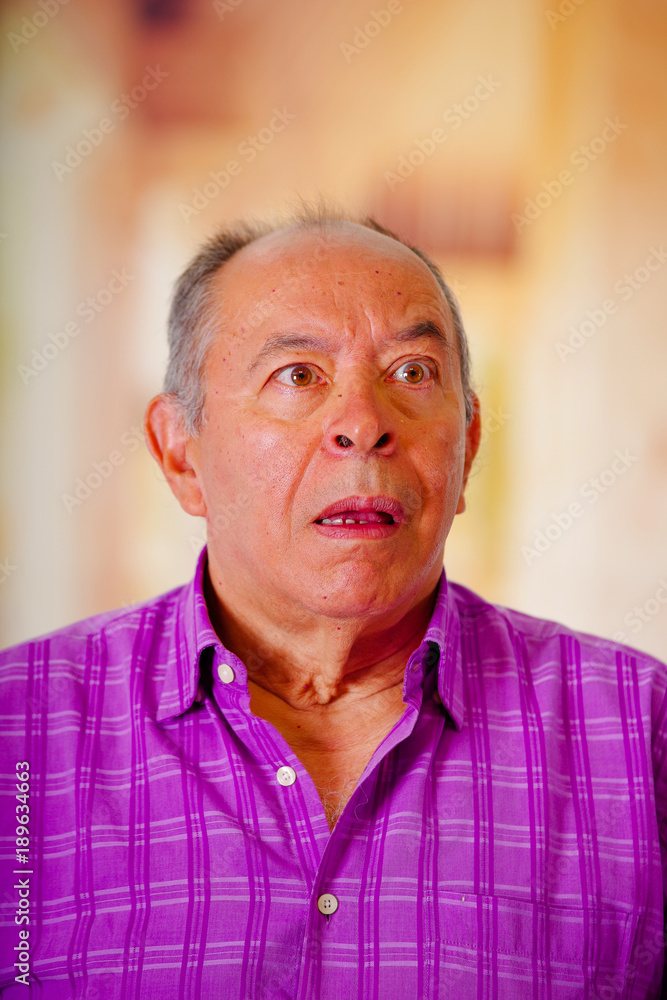 Portrait of a surprissed mature man, with his mouth open and wearing a purple square t-shirt in a blurred background Portrait of a surprissed mature man, with his mouth open and wearing a purple square t-shirt in a blurred background