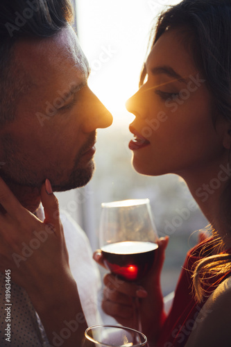 Young woman with glass of wine kissing her man in sunset