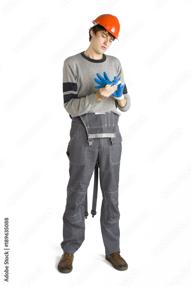 A young man in working grey clothes and orange hard helmet putting on a glove on white isolated background. A young man in working grey clothes and orange hard helmet putting on a glove on white isolated background.