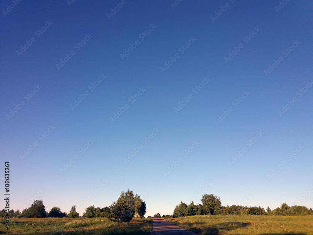 Fototapeta premium Background view of clear blue sky, meadow and a road at a low bottom. Sunny day, evening.