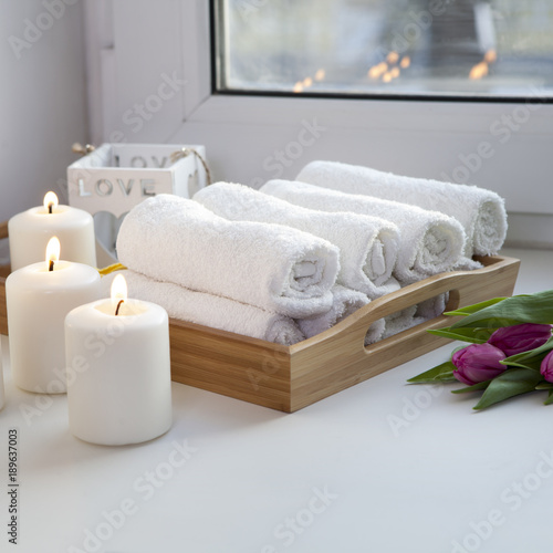 Fototapeta Naklejka Na Ścianę i Meble -  the Rolled hand towels on a tray next to the lighted candles and a bouquet of tulips in the spa salon