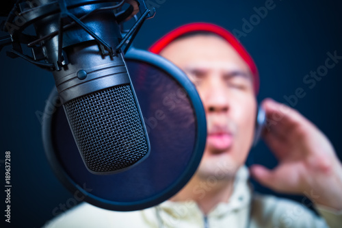 asian handsome male singer singing in recording studio or DJ chatting in radio station, nightclub. focus on condenser microphone
