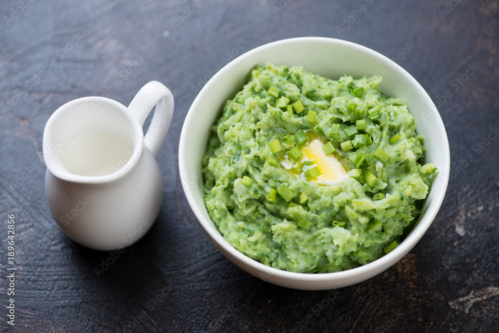 Irish colcannon or mashed potato with addition of kale, leek and green onion and topped with butter, dark brown stone background, studio shot Irish colcannon or mashed potato with addition of kale, leek and green onion and topped with butter, dark brown stone background, studio shot