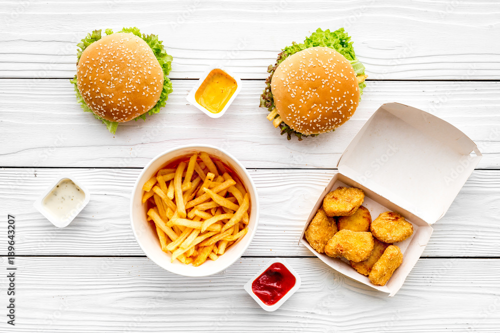 Most popular fast food meal. Chiken nuggets, burgers and french fries on white wooden background top view Most popular fast food meal. Chiken nuggets, burgers and french fries on white wooden background top view