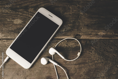 Close-up of smart phone with headphones on a Wood background. Listen to music. vintage Tone