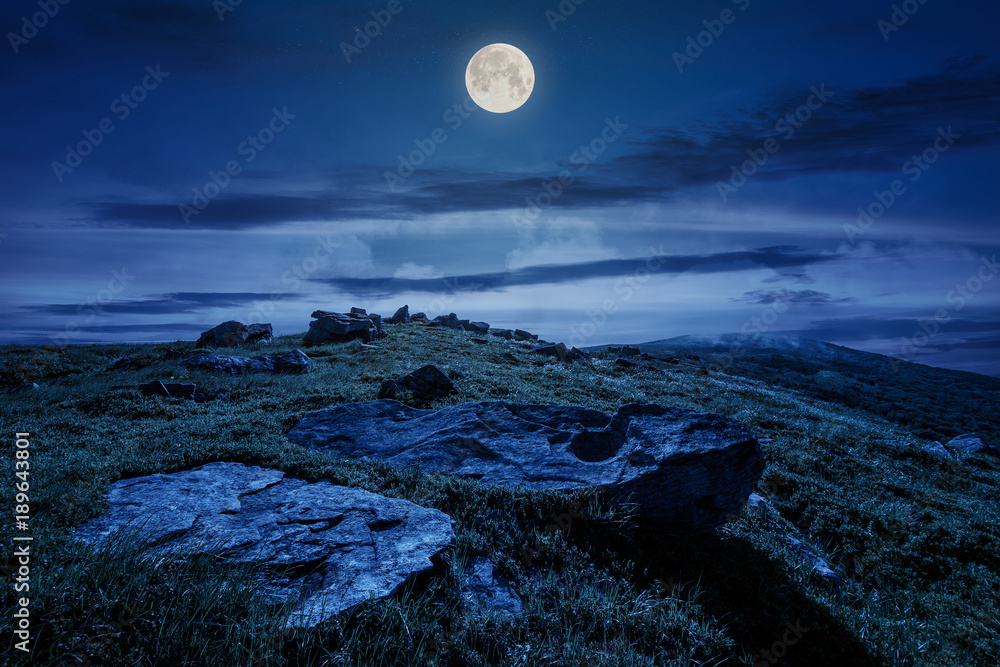 rocky formation on grassy hillside. beautiful scenery of Runa mountain in summertime at night in full moon light. location Carpathian mountains, Ukraine