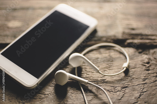 Close-up of smart phone with headphones on a Wood background. Listen to music. vintage Tone