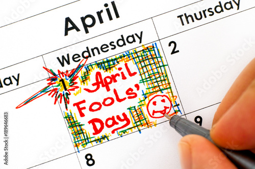 Woman fingers with pen writing reminder April Fools Day in calendar.