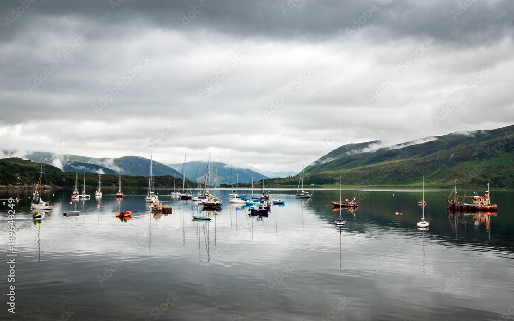 Fototapeta premium Boats moored on Loch Broom, Ullapool, Scotland. A view from Ullapool over the calm lake in the Scottish Highlands with overcast low cloud coverage.