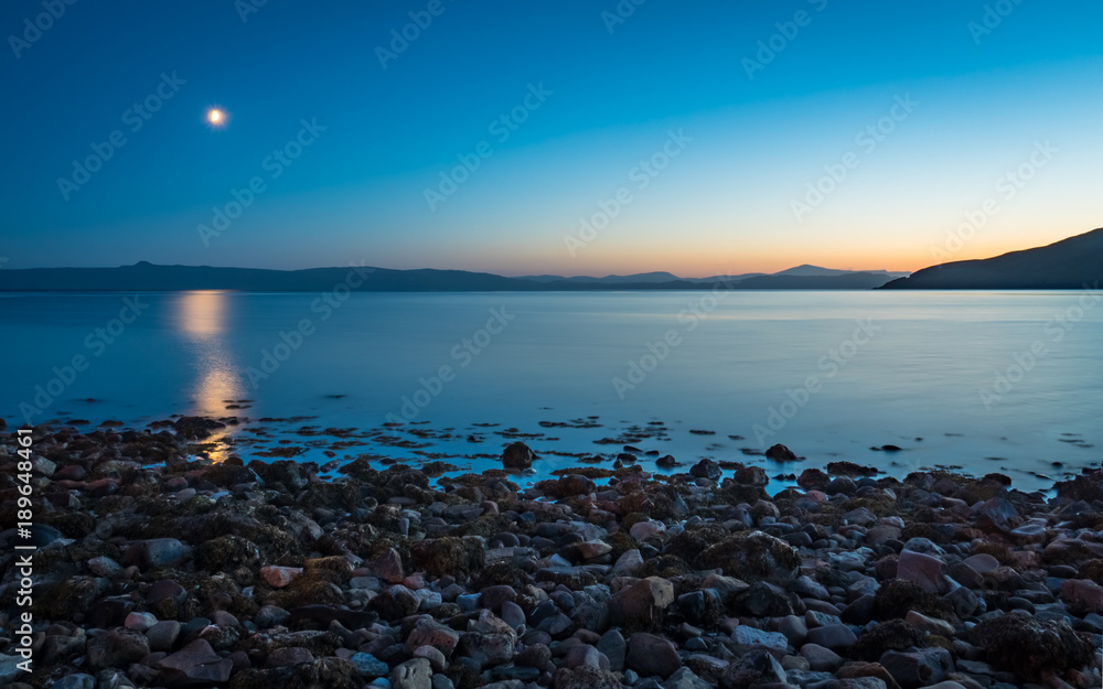 The Isle of Skye at dusk, Scotland. The moon rising and sun setting over the Isle of Sky, viewed from Applecross Bay on the Scottish west coast.