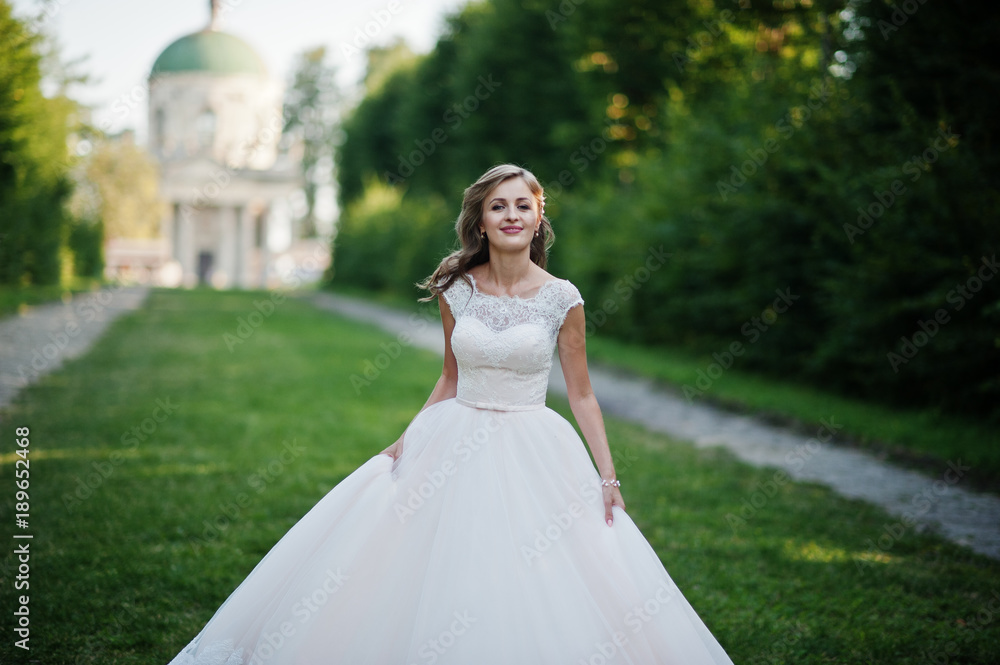 Lonely attractive bride walking on the green alley which leads to a church. Lonely attractive bride walking on the green alley which leads to a church.