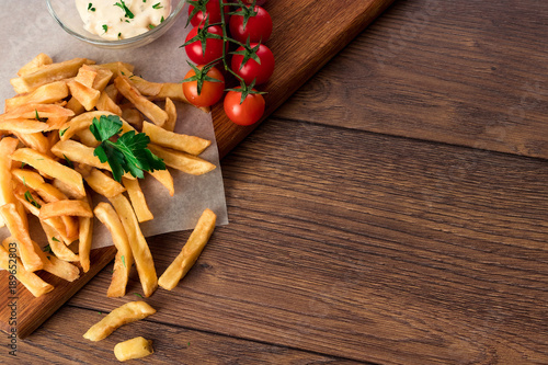 French fries, cherry tomatoes, garlic sauce on a wooden brown background, close-up. Fast food.