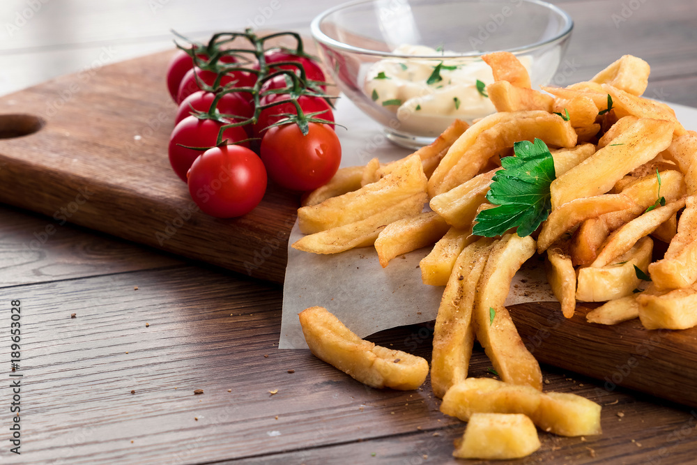 French fries, cherry tomatoes, garlic sauce on a wooden brown background, close-up. Fast food. French fries, cherry tomatoes, garlic sauce on a wooden brown background, close-up. Fast food.