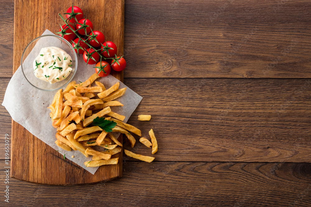 French fries, cherry tomatoes, garlic sauce on a wooden brown background, top view. Fast food. French fries, cherry tomatoes, garlic sauce on a wooden brown background, top view. Fast food.