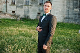 Portrait of a handsome groom standing on the grass next to the castle.