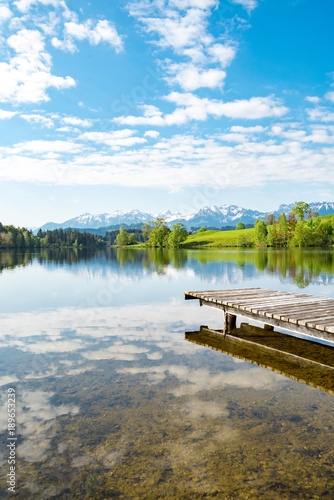 Idyllischer See mit Holzsteg am Füße der Alpen, Hochformat