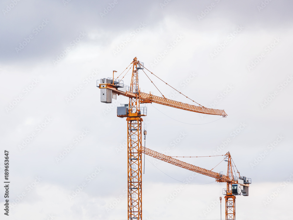Pair of construction cranes on cloudy sky background. Industrial machinery.