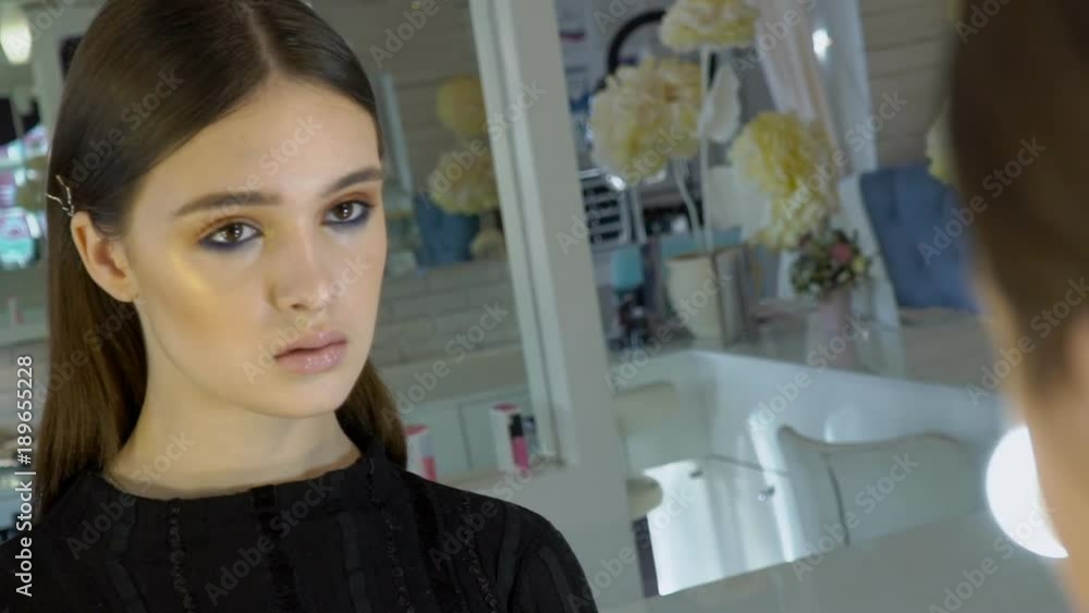 Portrait of young female model who is looking at her reflection in the mirror in studio. The brunette lady has a beautiful make-up and her dark eyes are very impressive with this colors. Big stylish Portrait of young female model who is looking at her reflection in the mirror in studio. The brunette lady has a beautiful make-up and her dark eyes are very impressive with this colors. Big stylish