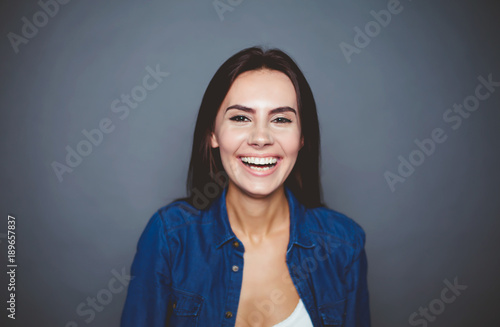 Portrait of a beautiful smiling modern girl in a denim shirt which poses in front of the camera on a gray background isolated.