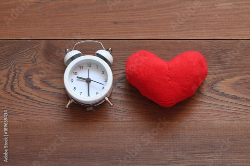 The white alarm clock and red plush heart on a wooden background