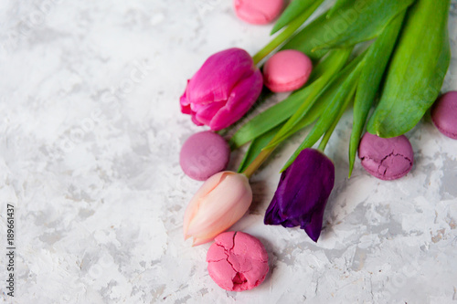 Pink and purple tulips and macarons on light textured background. Romantic congratulations concept with copy space.