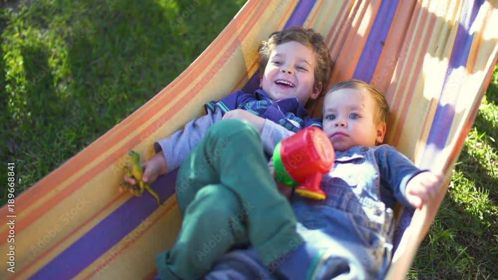 Two cute little brothers with blue eyes having fun in an hammock Two cute little brothers with blue eyes having fun in an hammock