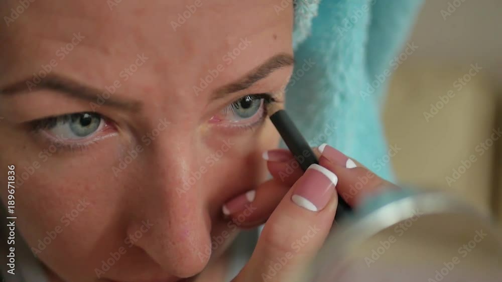 Close up portrait of a young woman with bath towel on head doing her make up looking at the mirror Close up portrait of a young woman with bath towel on head doing her make up looking at the mirror
