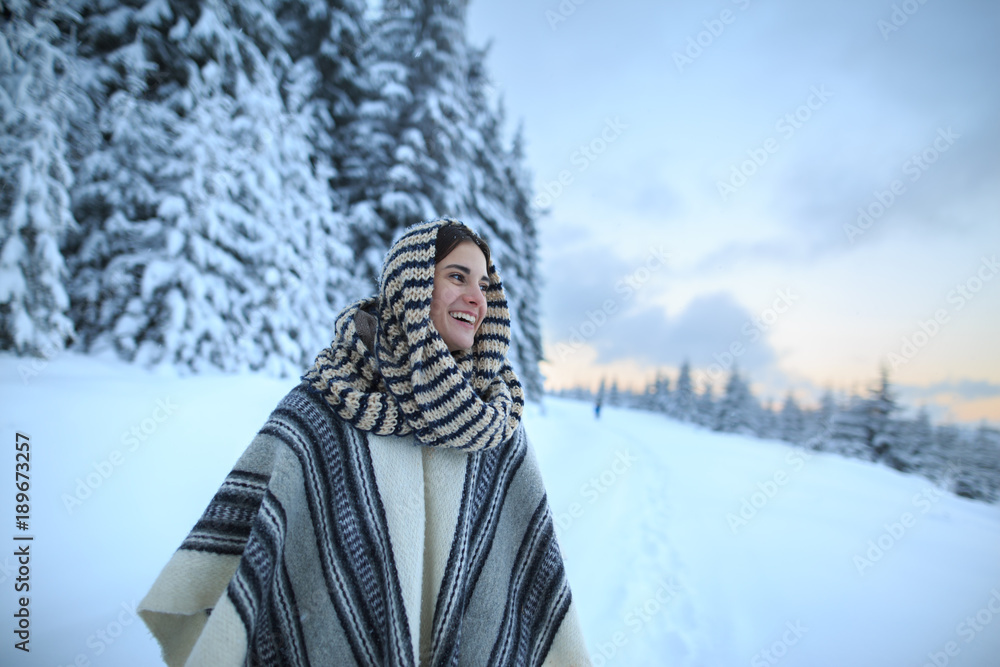 Fototapeta premium Young woman winter portrait. Happy young woman walking in winter forest. Happy girl having fun in the snow. Snow covered trees in the winter sun light. Snowy pine trees on a winter landscape