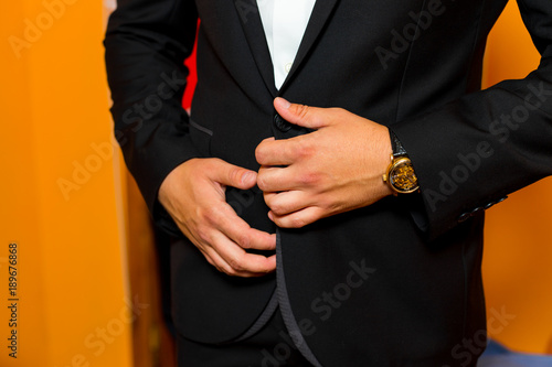 Groom in black suit getting ready in the morning. The young man fastens the buttons of the jacket, close-up