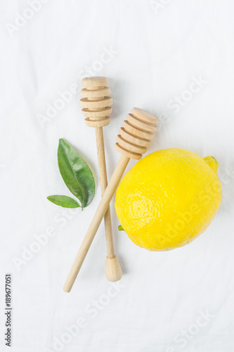 Wooden Honey Dippers Ripe Yellow Lemon Green Citrus Leaves on White Cotton Linen Fabric Background. Organic Cosmetics Ayurveda Healthy Lifestyle Concept. Copy Space