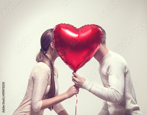 Valentine's day. Happy joyful couple holding heart shaped air balloon and kissing. Love