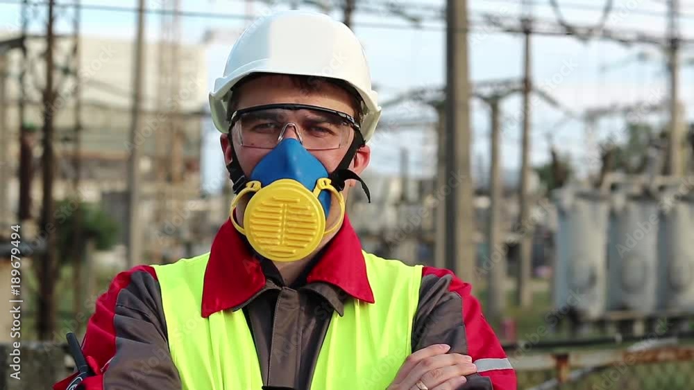 Worker in respirator on electric power station looks at the camera. Power engineering specialist in gas mask, goggles and hard hat at heat power plant Worker in respirator on electric power station looks at the camera. Power engineering specialist in gas mask, goggles and hard hat at heat power plant