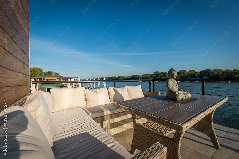 Big sofa on terrace by the river and Buddha sculpture on table