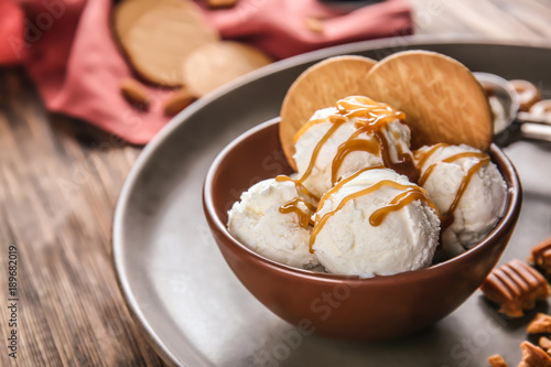 Bowl of ice cream with caramel sauce and cookies on table