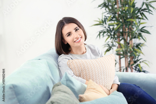 Beautiful smiling woman with pillow sitting on sofa in room