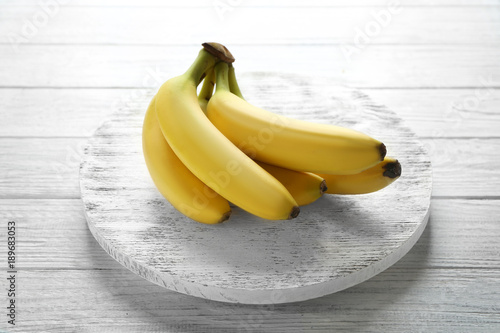 Board with ripe bananas on white wooden background