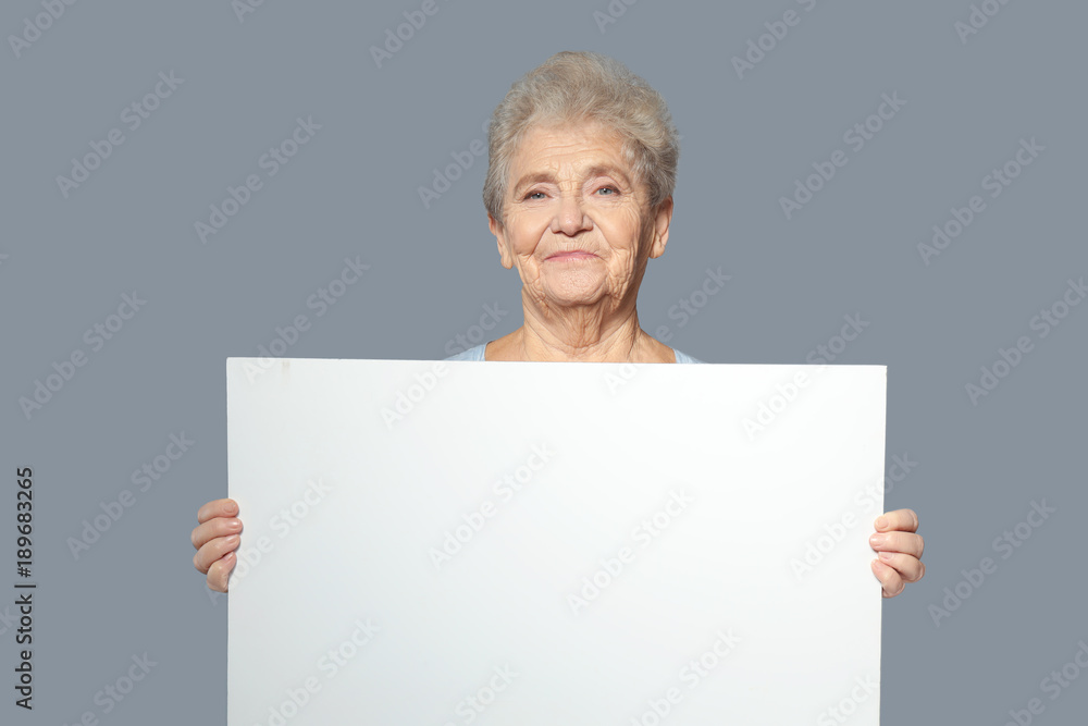 Senior woman with blank advertising board on grey background Senior woman with blank advertising board on grey background